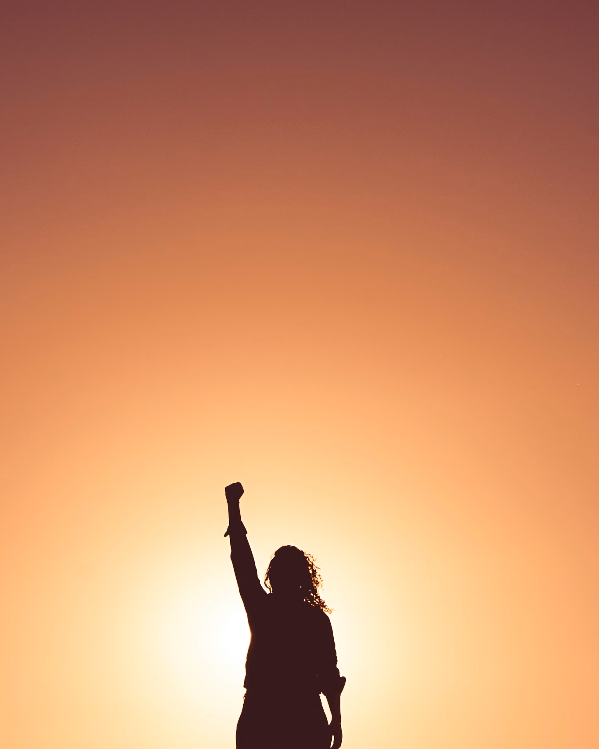 woman silhouetted against sunset with fist raised in air