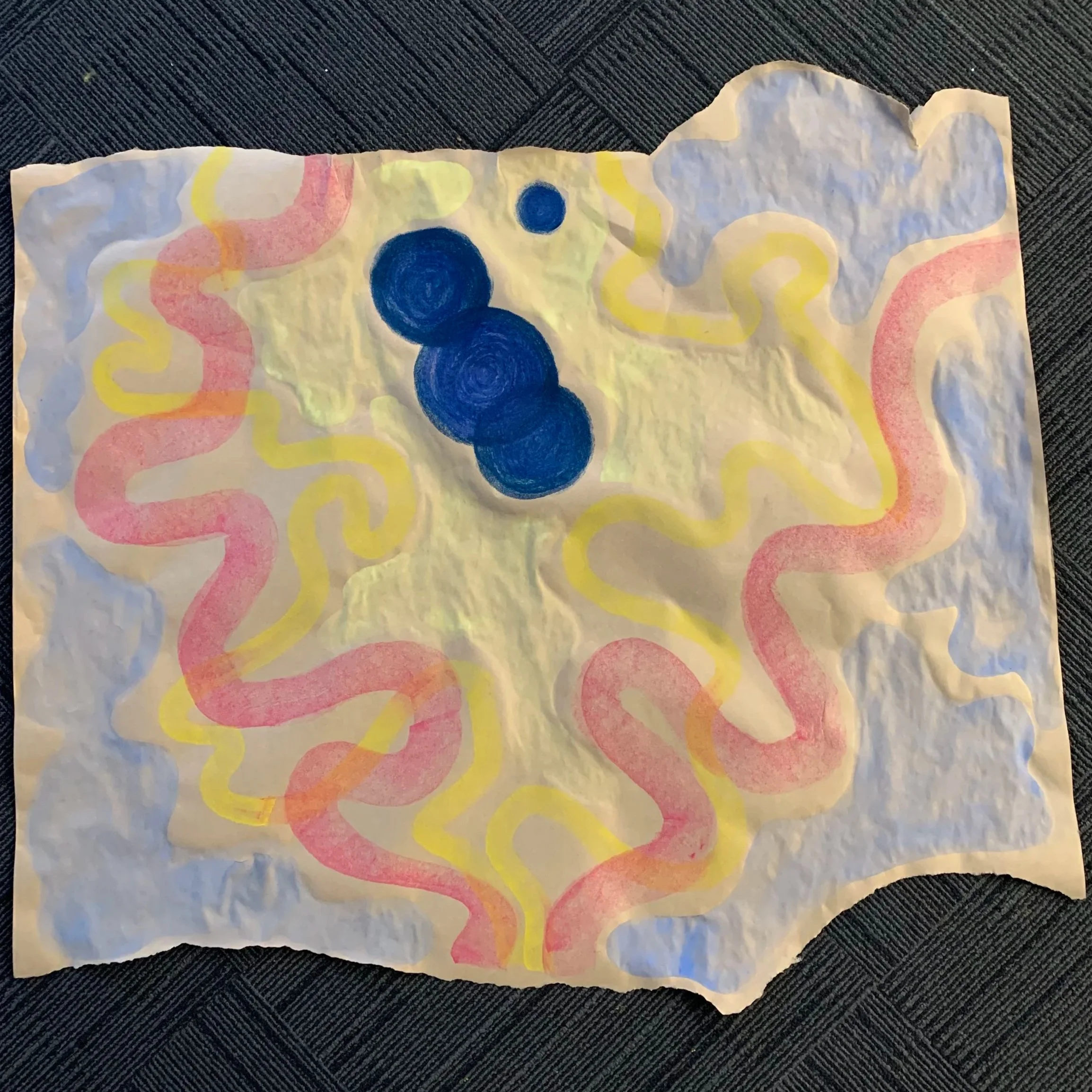 A piece of crumpled white paper with abstract paint design, featuring blue circles in the center and pink, yellow, and light blue squiggly lines around the edges.