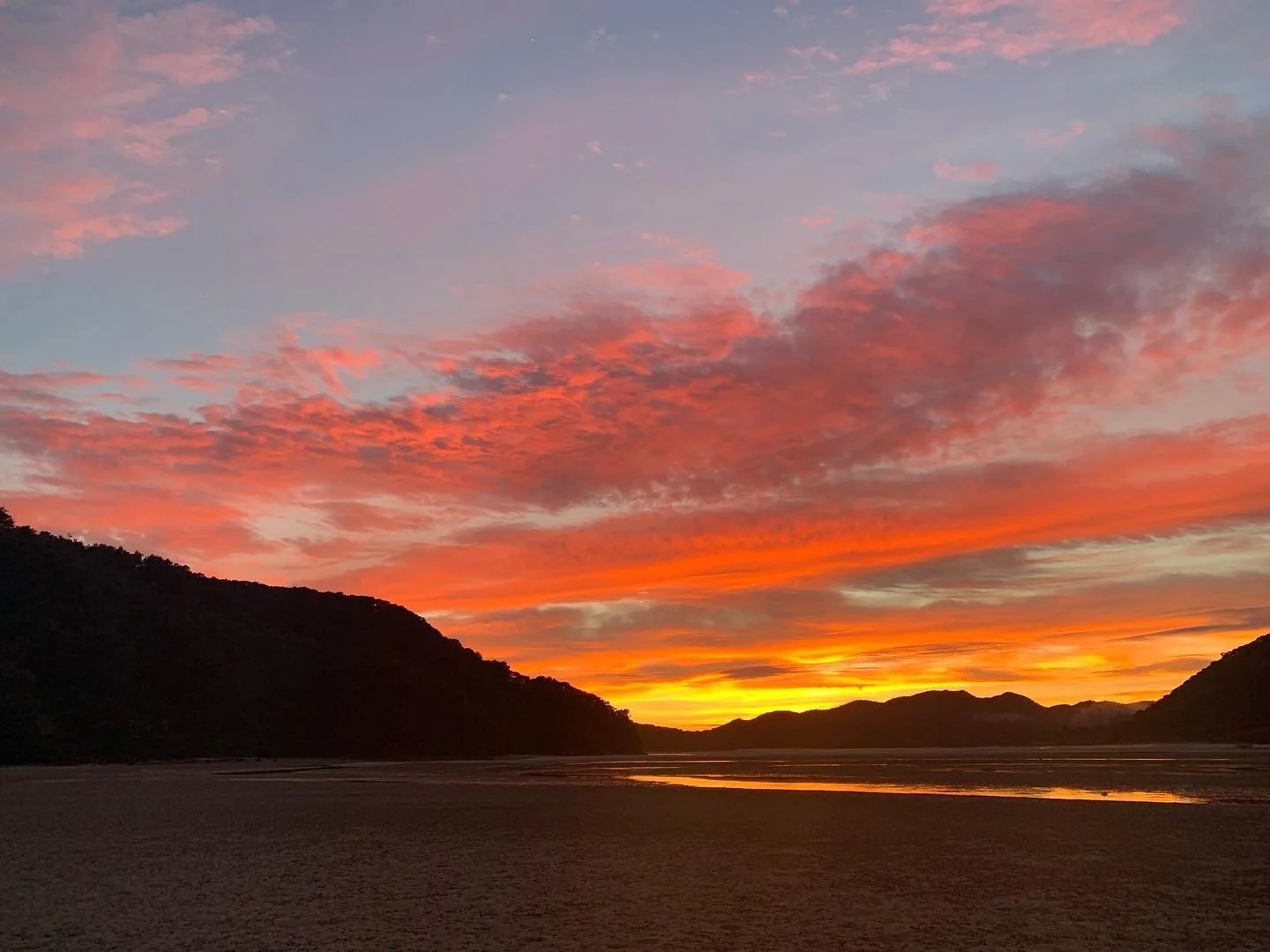 Sunset over a river valley with colorful clouds in orange, pink, and purple hues, silhouetted hills on either side.