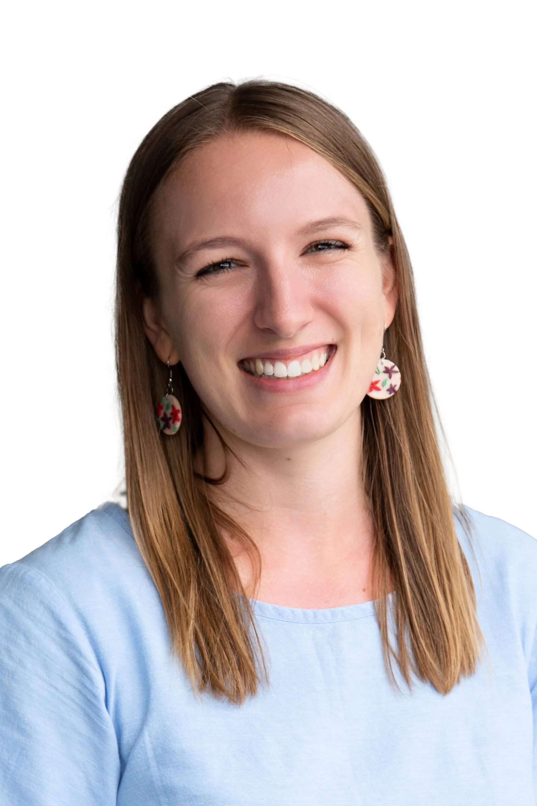 A woman with straight, shoulder-length brown hair wearing a light blue top, smiling, with earrings featuring colorful floral designs, against a plain white background.