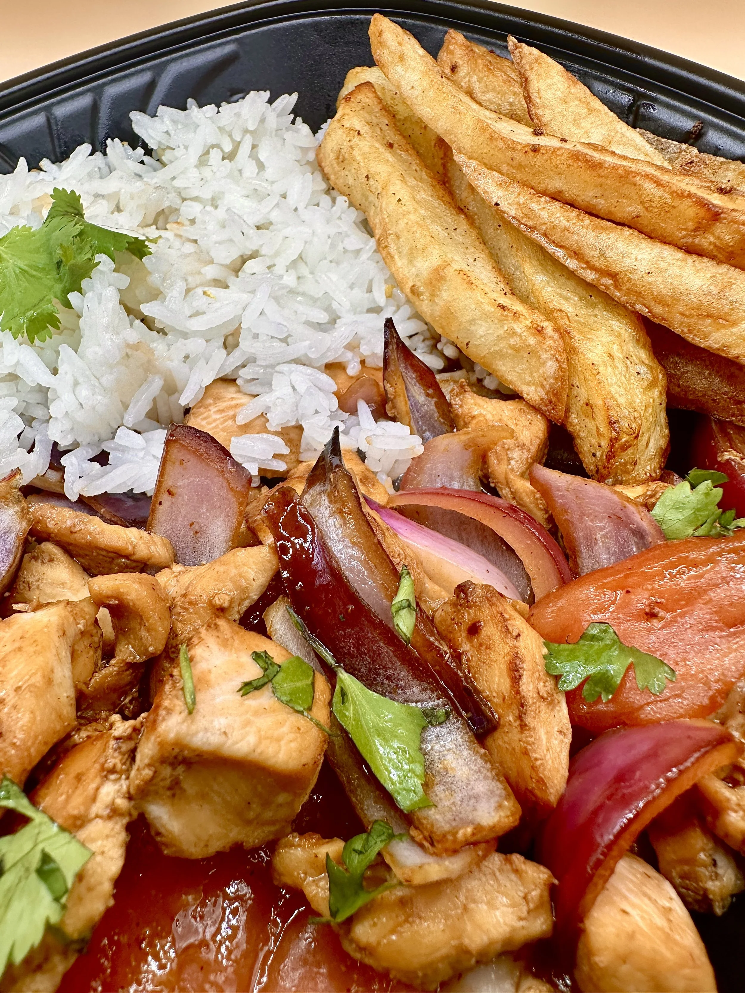 Lomo Saltado De Pollo - grilled chicken, sautéed red onions and with cilantro, all on a black tray.