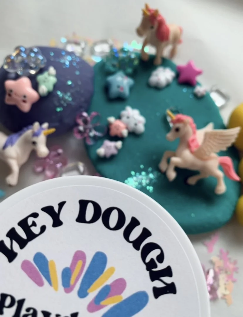 Colorful playdough with unicorn toys, star and cloud-shaped decorations, and glitter on a surface.