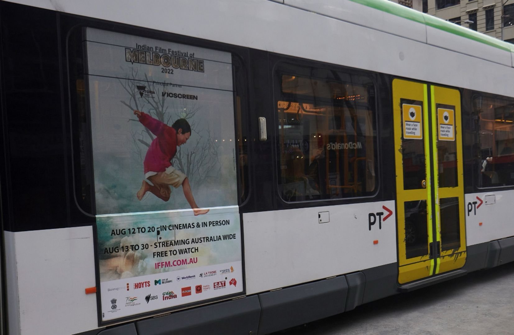 Poster on tram advertising the Indian Film Festival of Melbourne 2022, showing a child jumping with a background of trees and water, with event details and website.