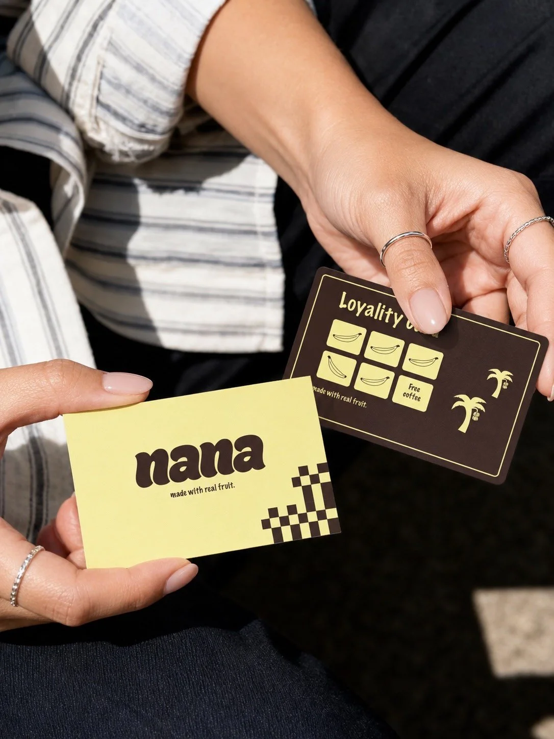Two hands holding loyalty cards: one yellow card with the word 'nana' and a checkered design, and one black card with banana icons and text about loyalty benefits.