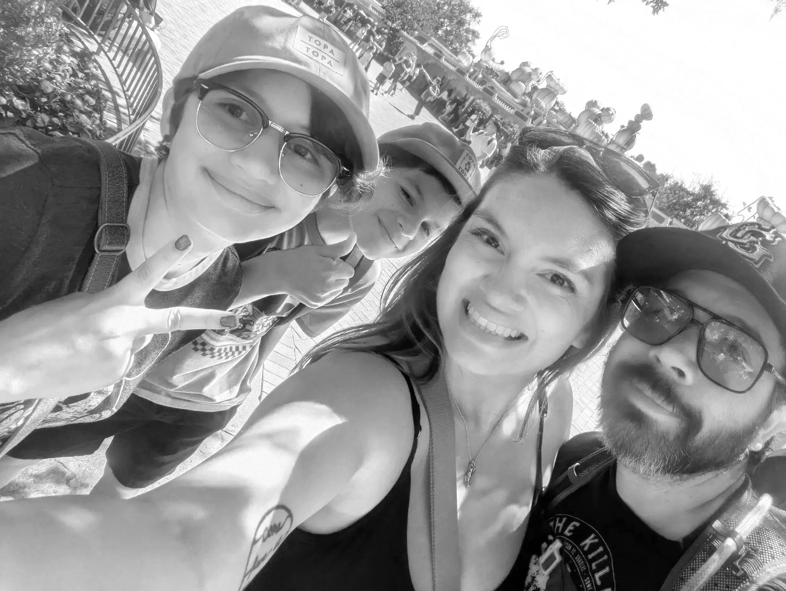 Four people taking a selfie at an amusement park with a carousel in the background, smiling and making peace signs.