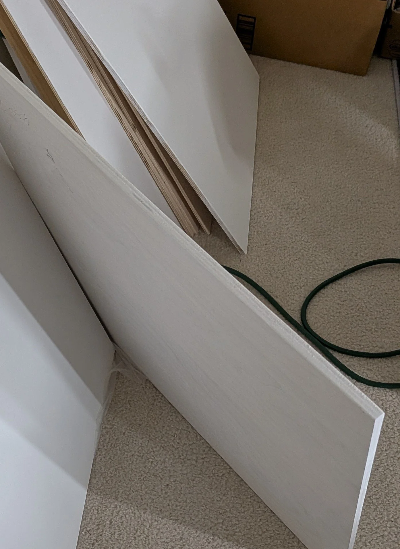Various pieces of white painted wood paneling and molding laid on a beige carpeted floor, with some boxes and a green electrical cord in the background.