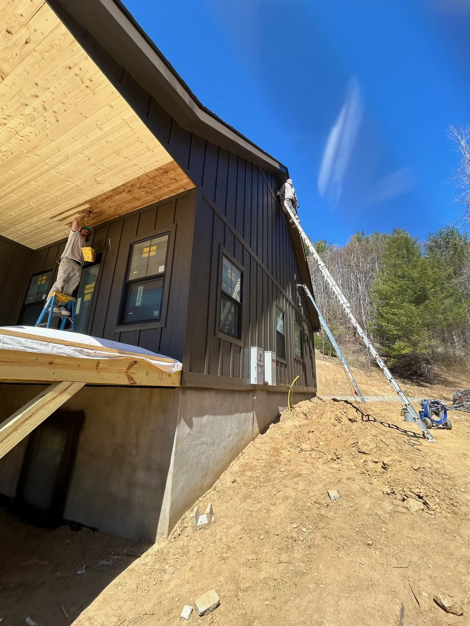 Construction workers installing wooden panels on the exterior of a house under a bright blue sky.