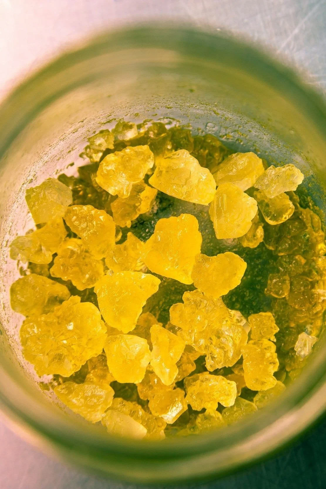 Close-up of yellow crystallized rocks inside a glass jar from above view.
