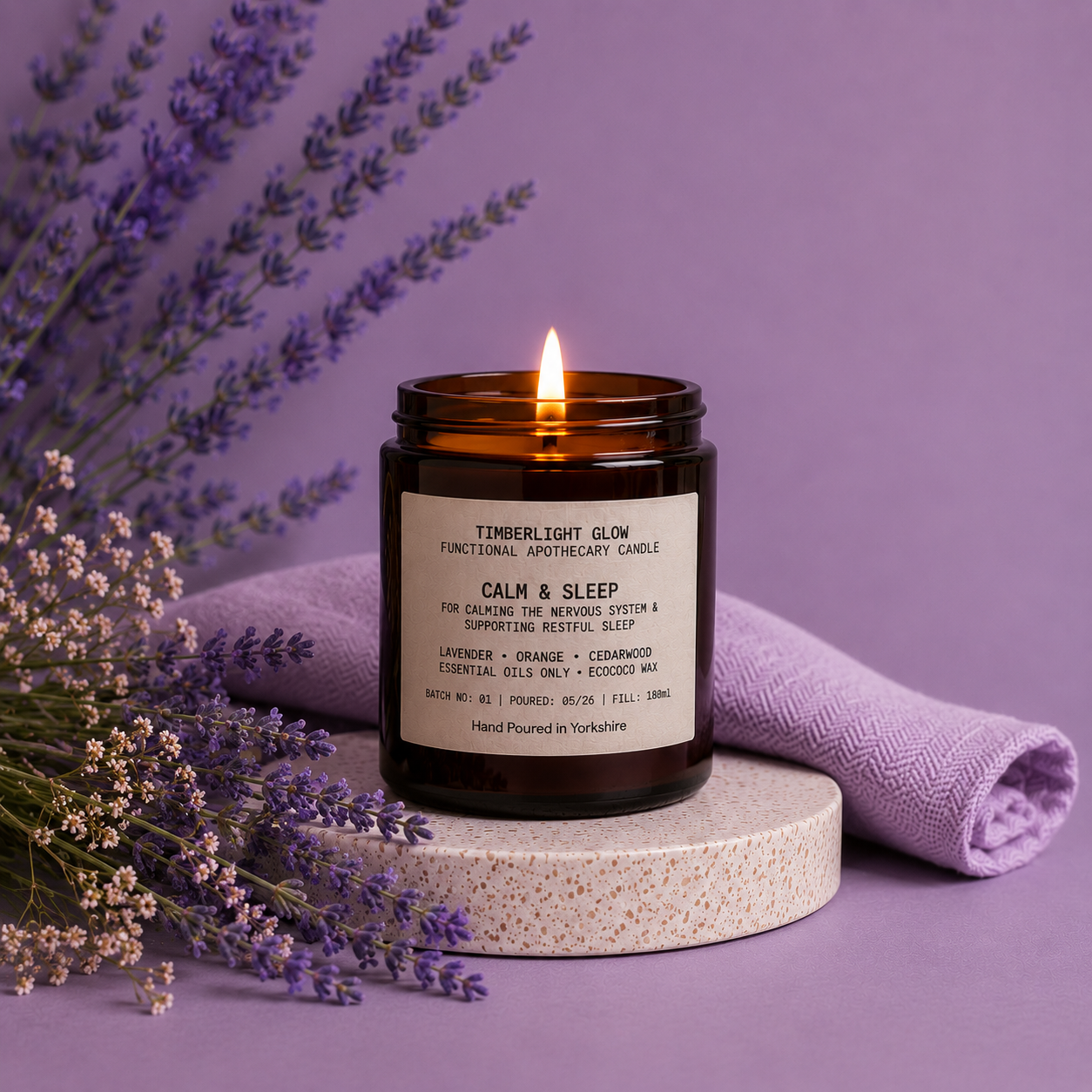 Lit TimberLight Glow Calm & Sleep aromatherapy candle with lavender sprigs on a soft purple background.