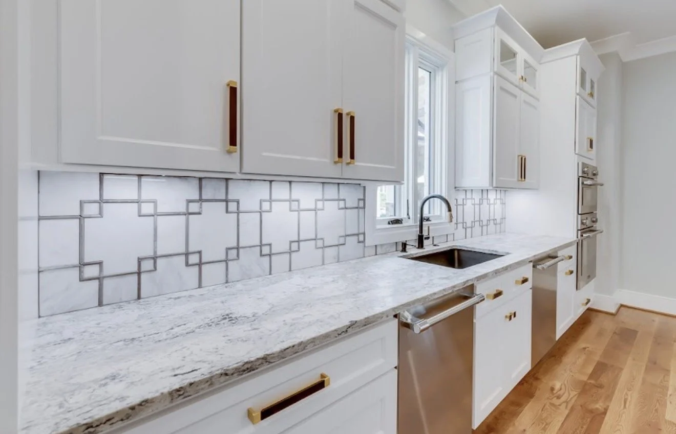 A modern kitchen with white cabinets, marble countertops, a black sink, and gray geometric tile backsplash.