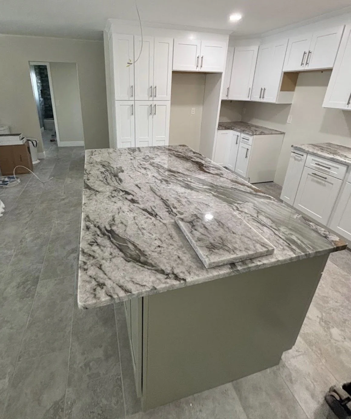 A kitchen with white cabinets, granite countertops, and an island with matching granite surface.