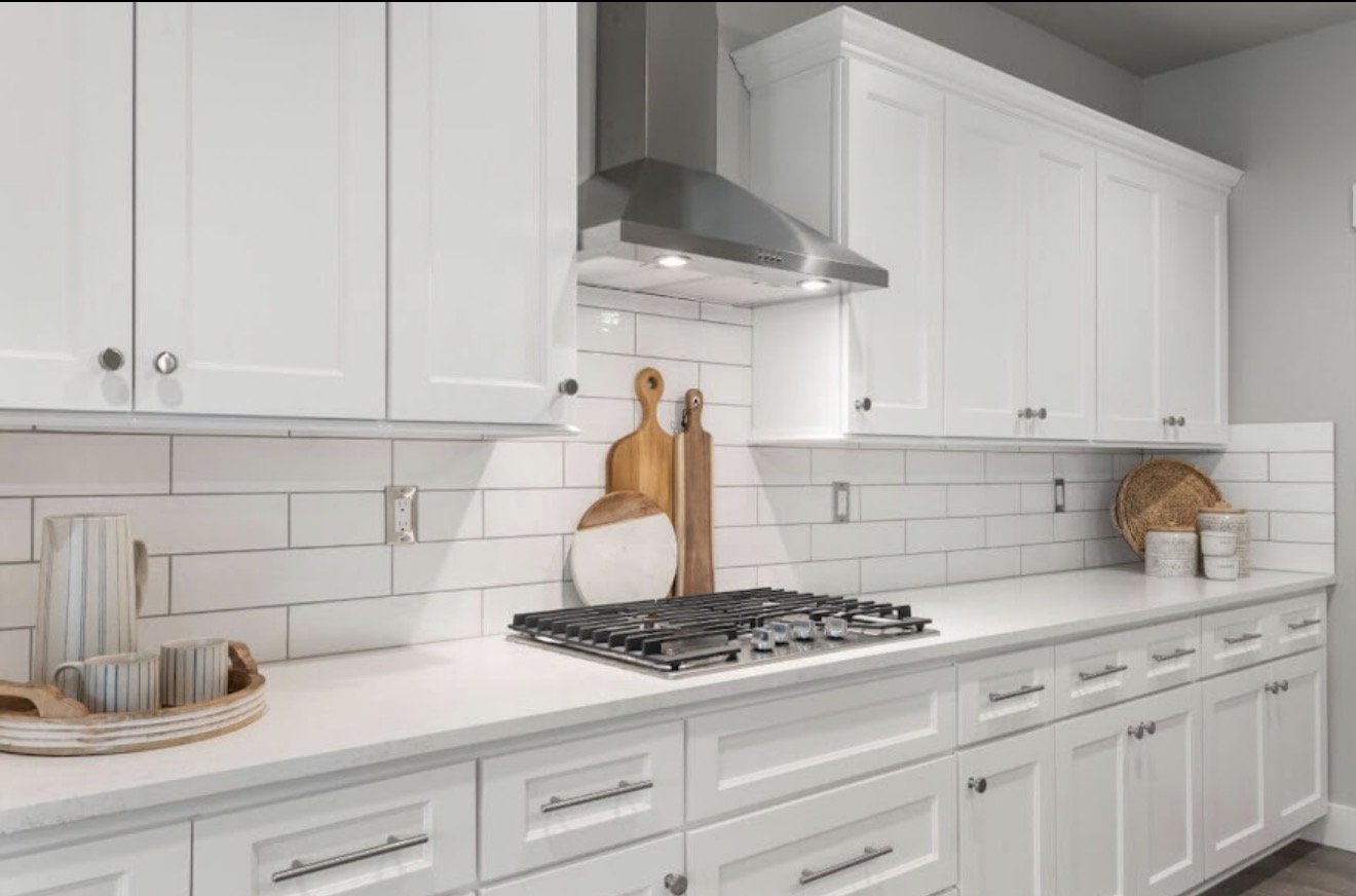 White kitchen with cabinets, a gas stove, a stainless steel range hood, and decorative items like cutting boards and baskets.