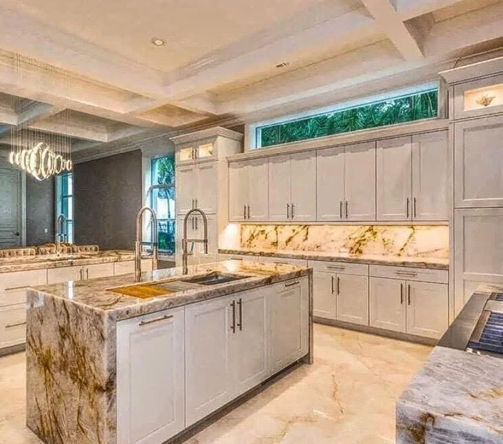 Modern kitchen with marble countertops, white cabinets, and a central island with a sink and faucet.