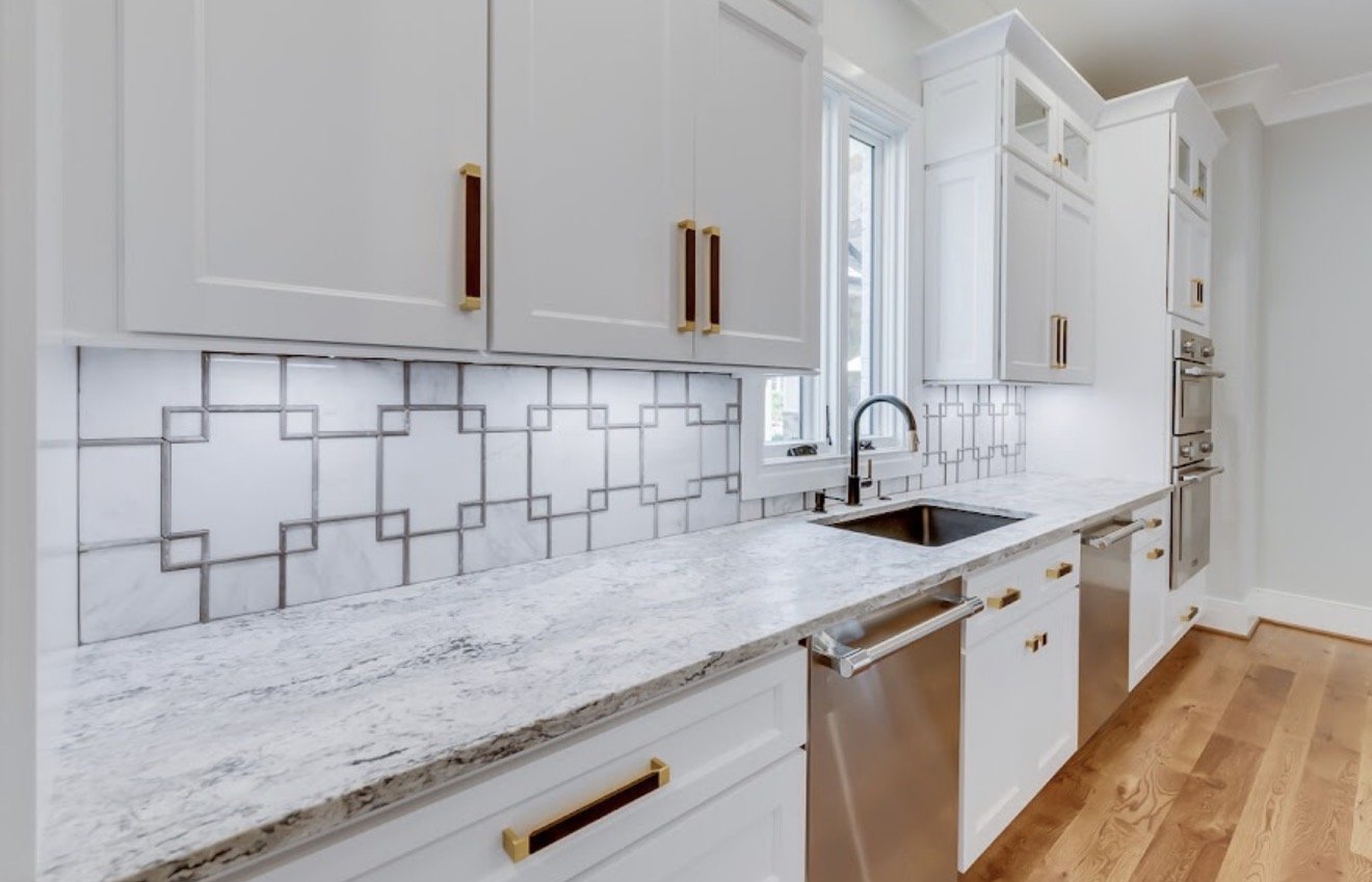 Modern kitchen with white cabinets, a marble countertop, gray geometric tile backsplash, and a black faucet above the sink.