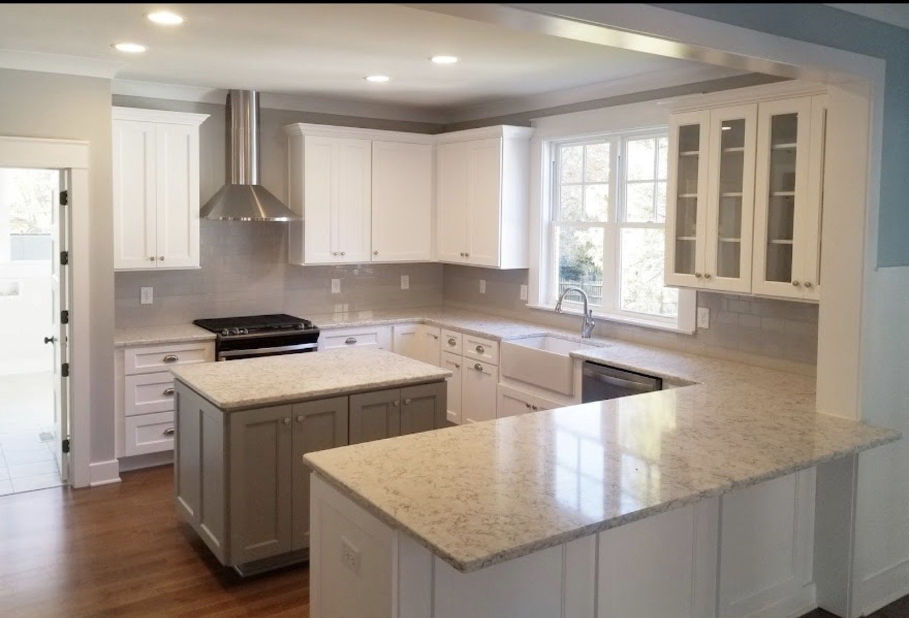 Modern kitchen with white cabinets, granite countertops, a central island, stainless steel range hood, and a double window over the sink letting in natural light.