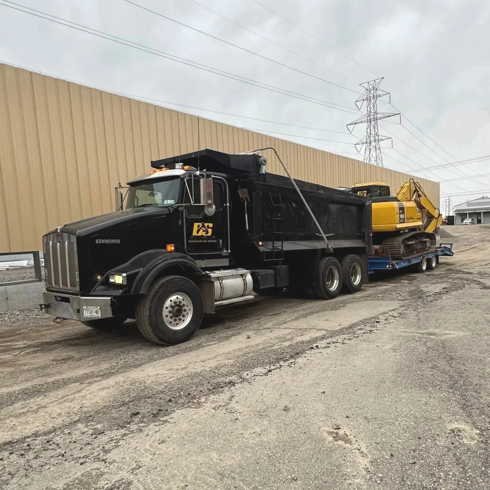 Our black Kenworth construction truck carrying a yellow excavator on a flatbed trailer.