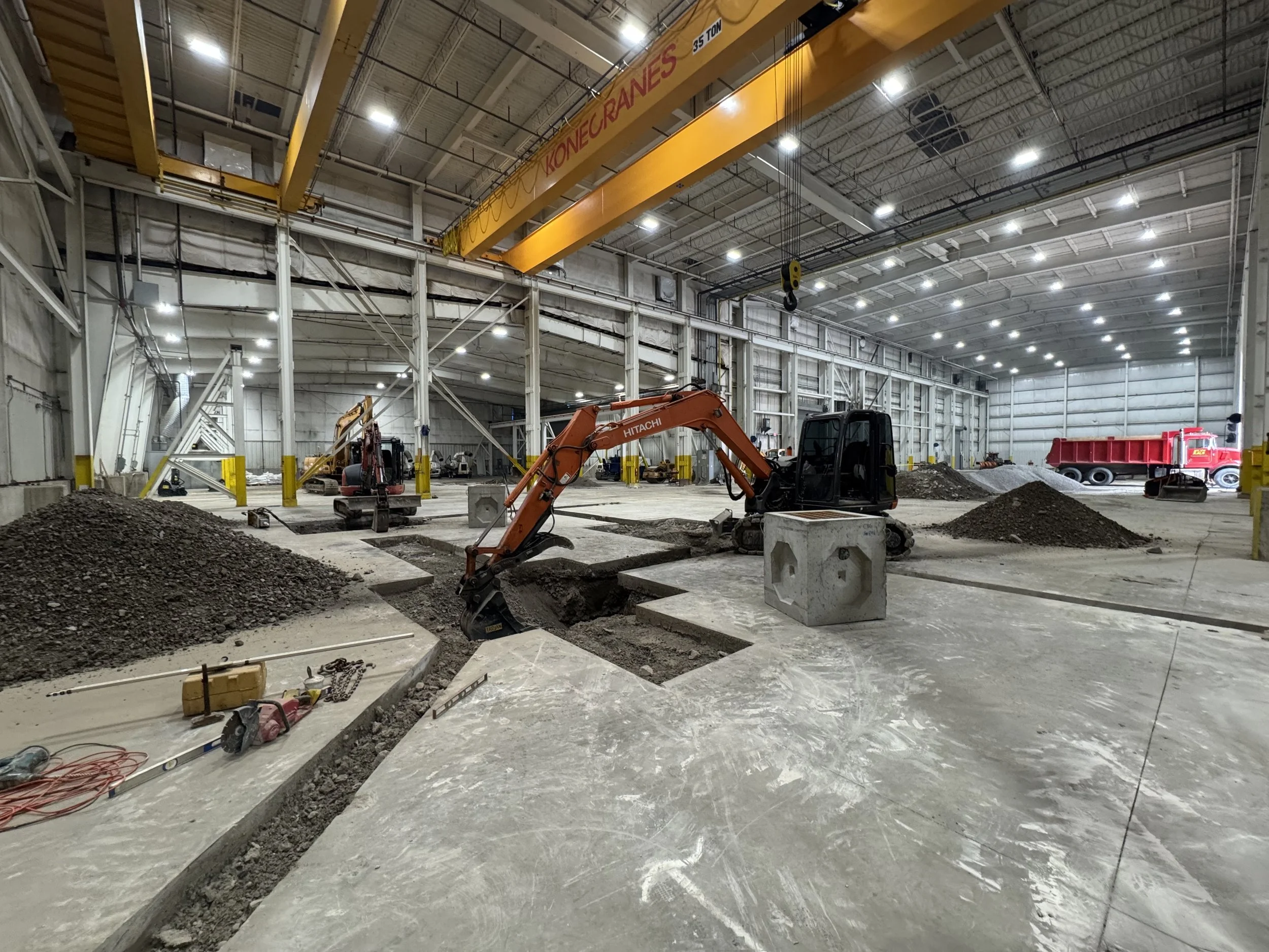 Inside a large industrial warehouse under construction with construction equipment and piles of gravel.