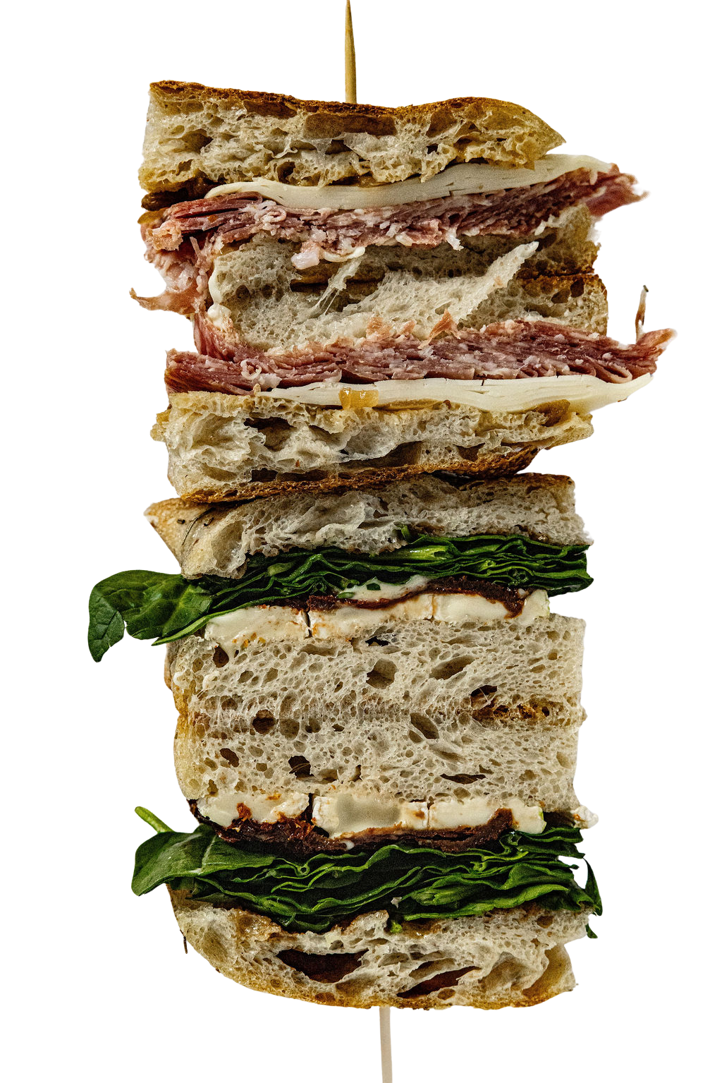 Cross-section of a sandwich stacked with various meat, cheese, and vegetable layers, including basil leaves.