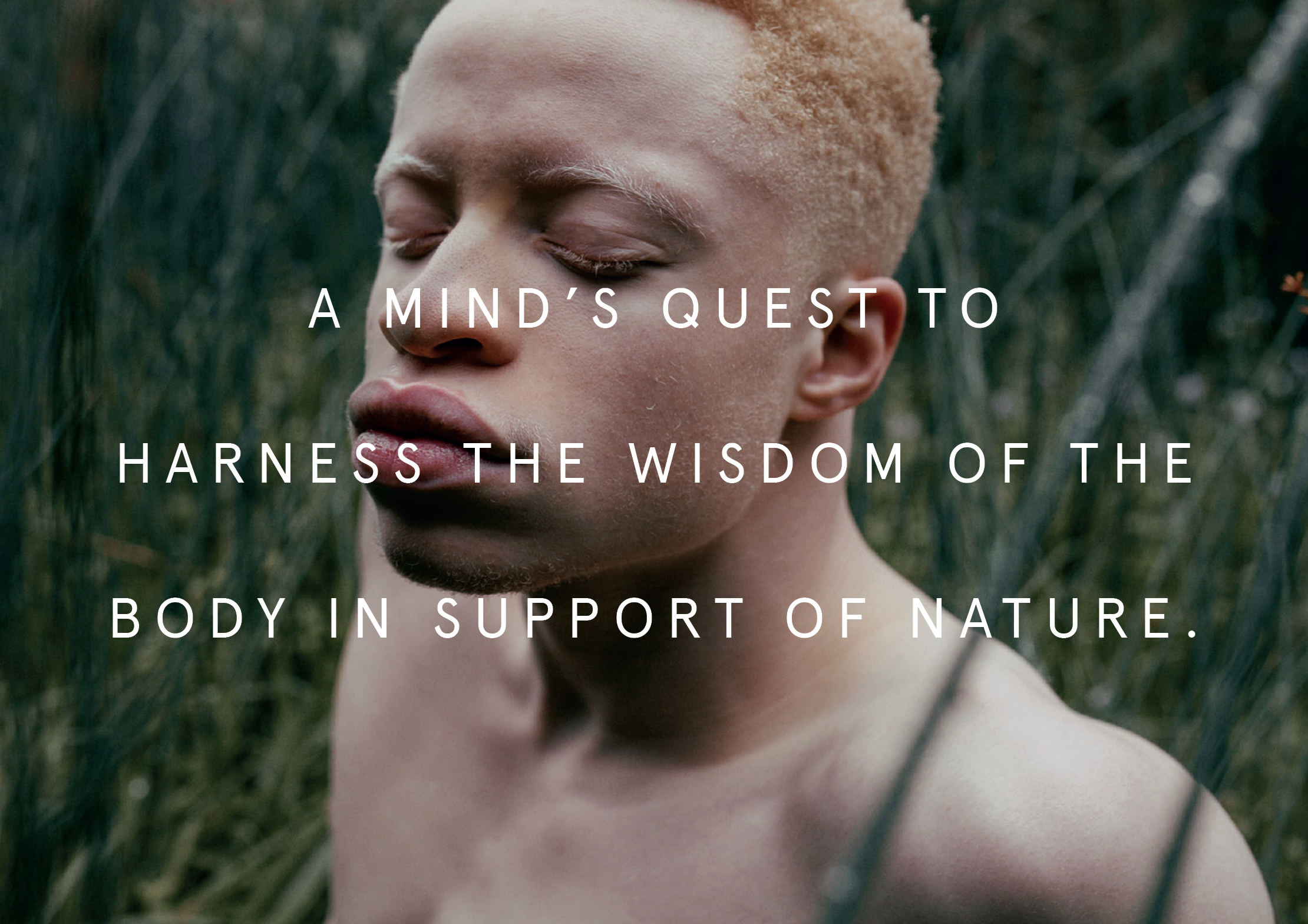 Close-up of a person's face with closed eyes, outdoors in a natural setting with green grass.