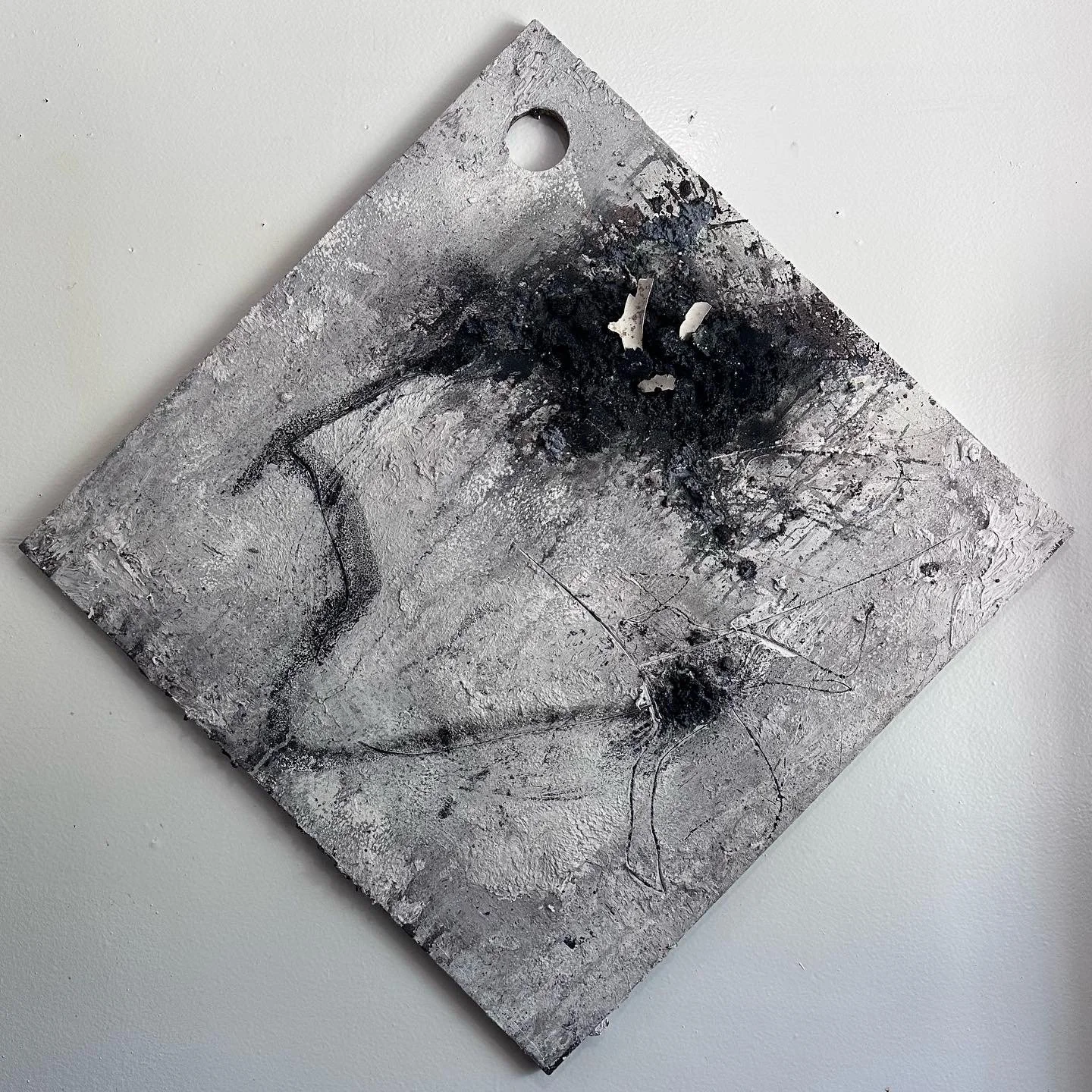 Abstract artwork with black and white paint splatters and textured surface, mounted on a wall at an angle.