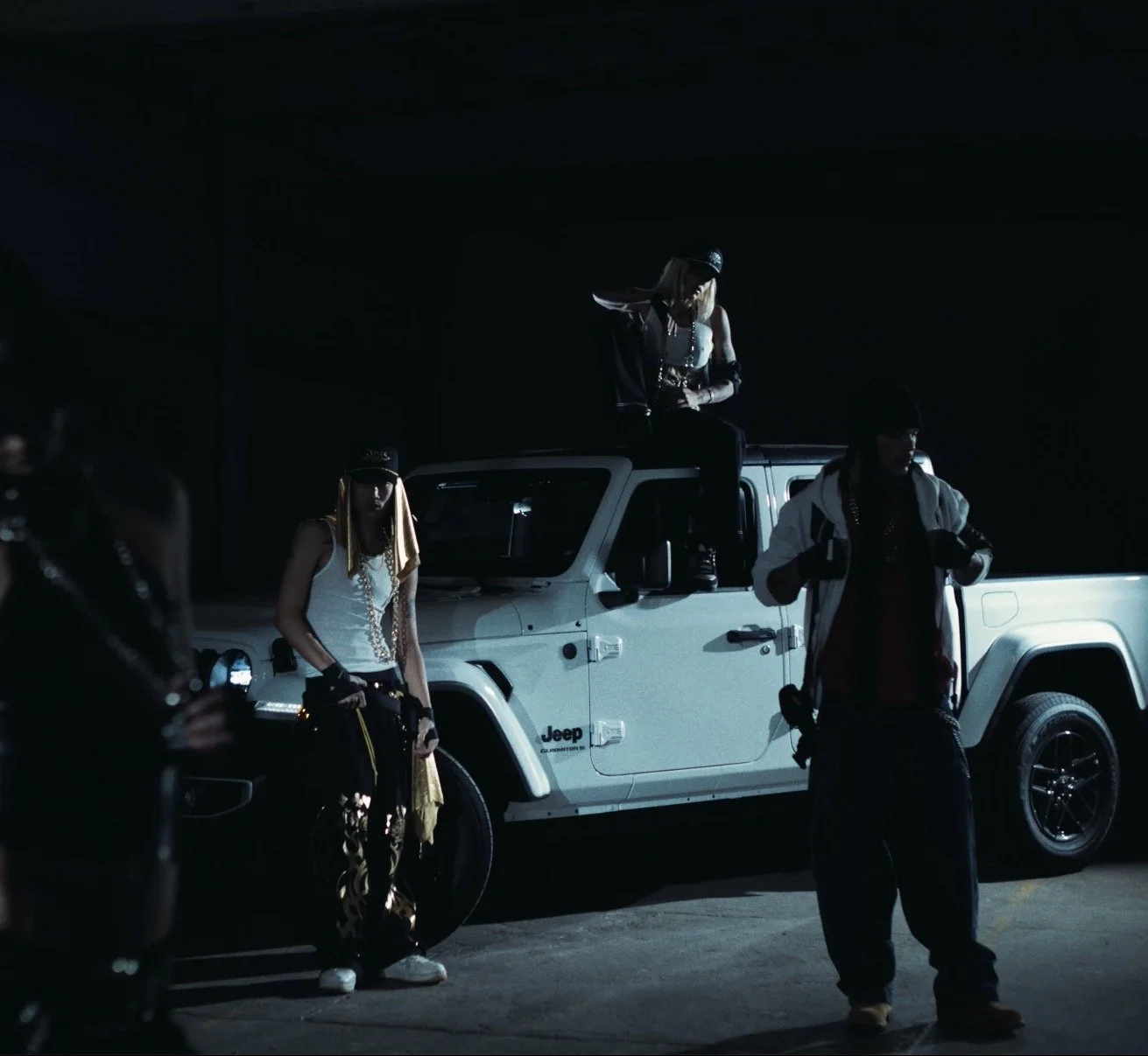 Individuals dressed in hip-hop fashion posing at night around a white Jeep truck in a dark setting.