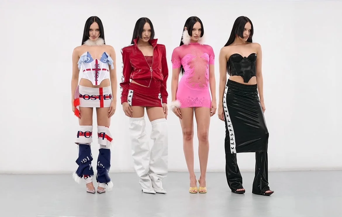 Four women standing against a plain gray backdrop, dressed in colorful, high-fashion outfits with various textures and styles, including dresses, skirts, and accessories.