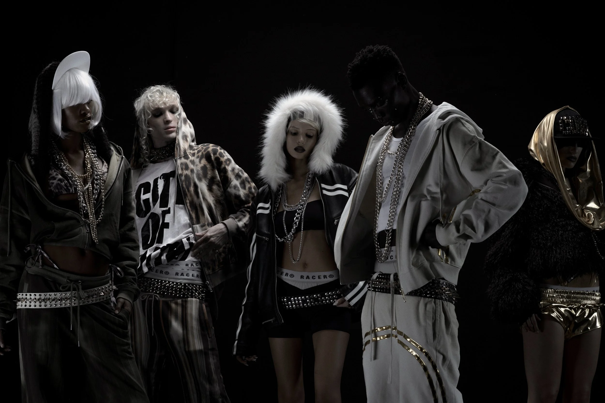 Group of five models dressed in designer streetwear with edgy accessories, standing in a dark setting.