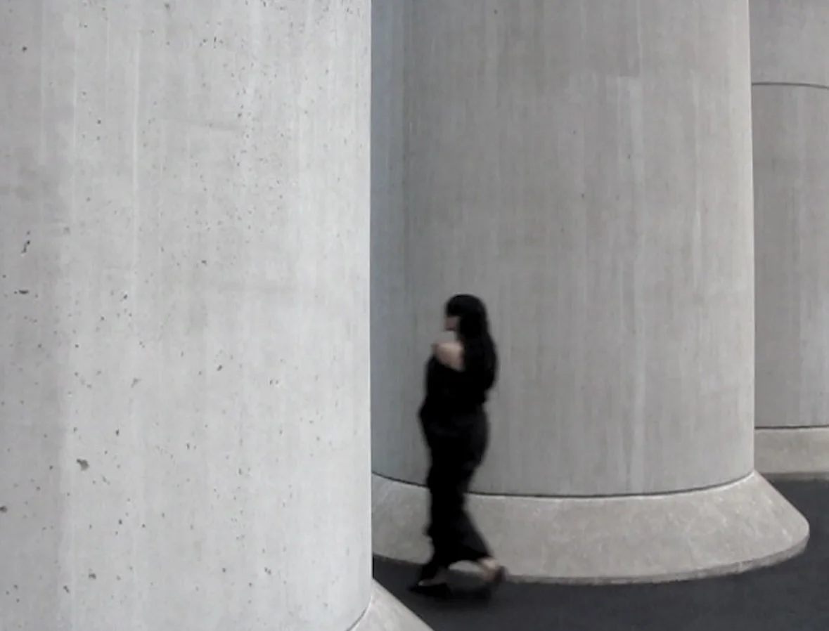 A woman skateboarding past large concrete columns in an indoor setting.