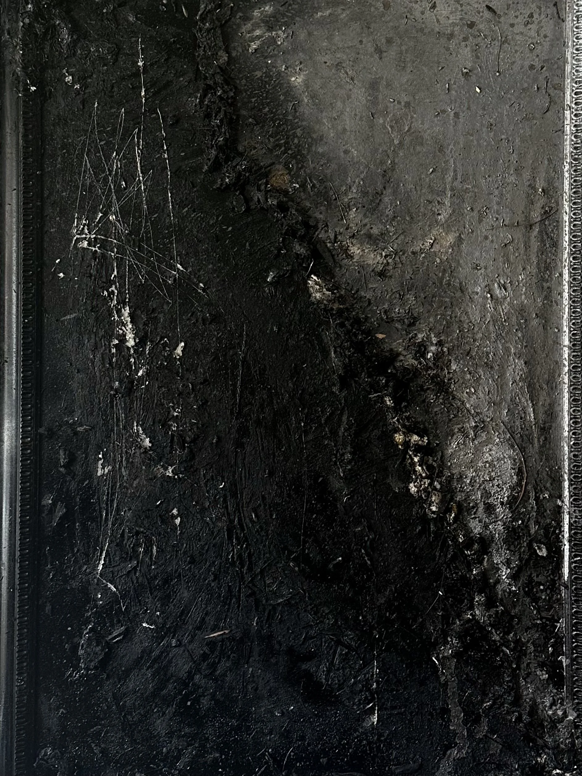 Close-up of a blackened, charred surface with scratches and burns, possibly a burnt piece of material or surface damage from fire.