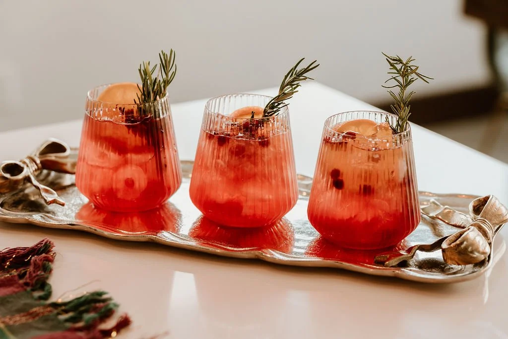 Three glasses of pink cocktail garnished with rosemary sprigs on a silver tray.