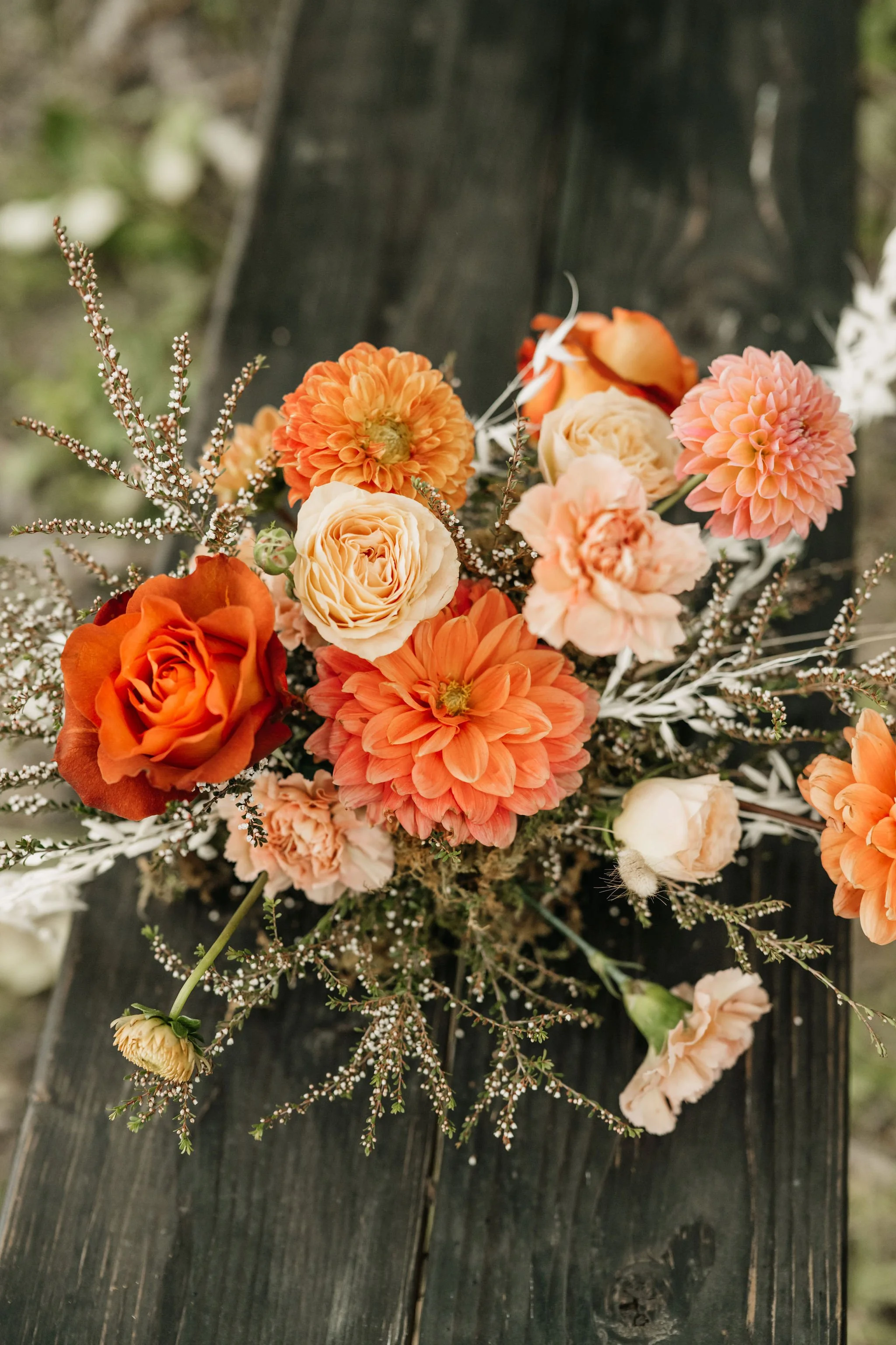 A bouquet of orange, peach, and cream-colored flowers on a dark wooden surface.