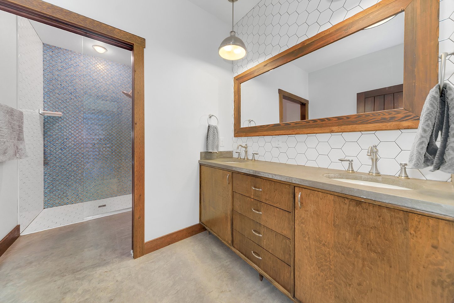 Bathroom with a wooden vanity and large mirror, hexagonal tile backsplash, and a walk-in shower with textured glass door.
