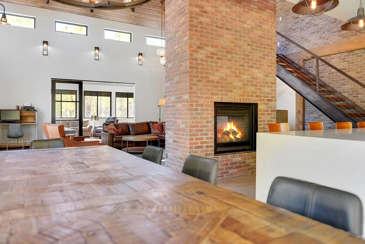 Interior view of a modern living space with a fireplace, brick walls, a large wooden table, and various seating areas.
