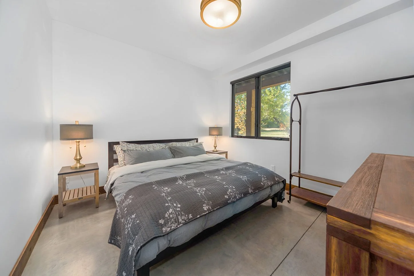 Bedroom with a bed, nightstands with lamps, a window showing trees outside, and a wooden dresser.