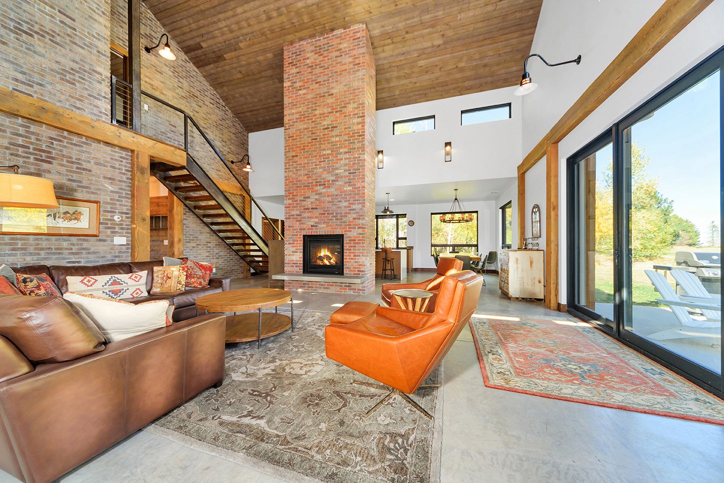 Living room with brick and wood accents, a fireplace, leather and fabric chairs, a large sliding glass door, and views of a backyard with outdoor chairs.