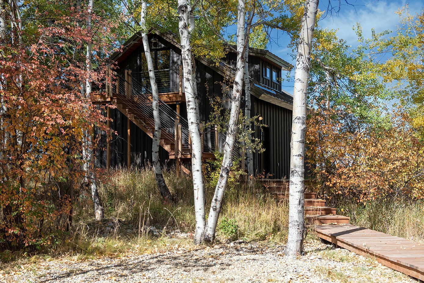 A detached king studio with a wooden staircase and a walkway surrounded by trees in fall foliage.