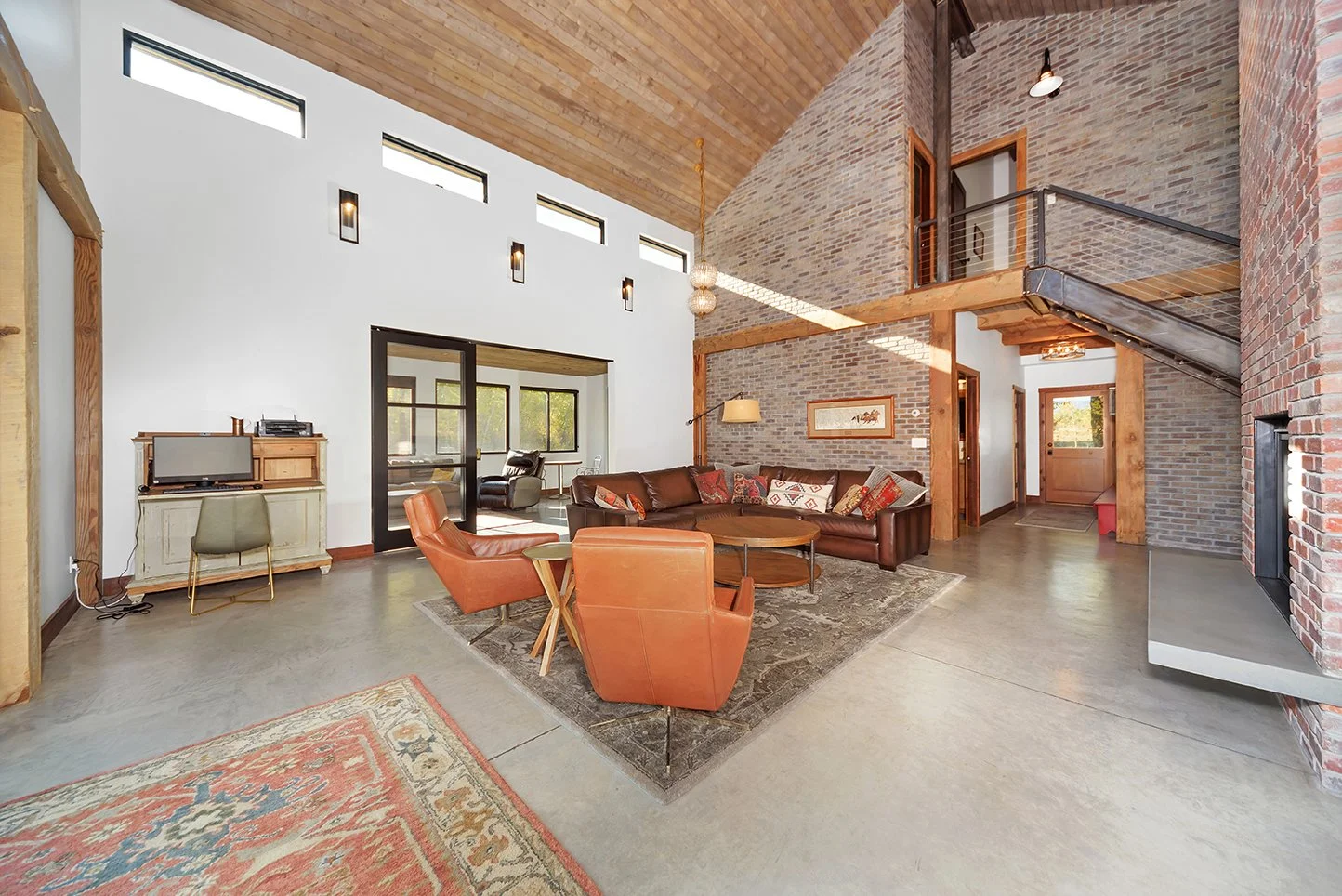 Living room with leather sofa, armchairs, wooden coffee table, brick walls, and wooden ceiling beams in a cozy, rustic style.
