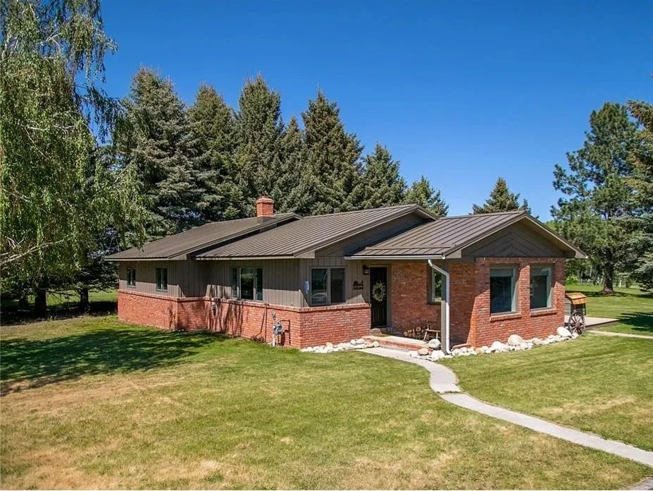 A single-story house with a brick and gray siding exterior, surrounded by a well-kept lawn and trees, under a clear blue sky.