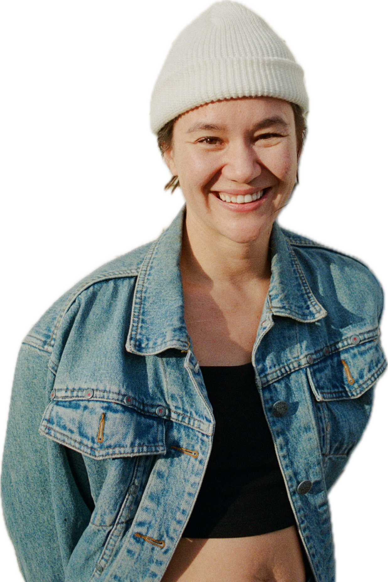 A smiling woman wearing a white beanie, denim jacket, and black top, standing outdoors.