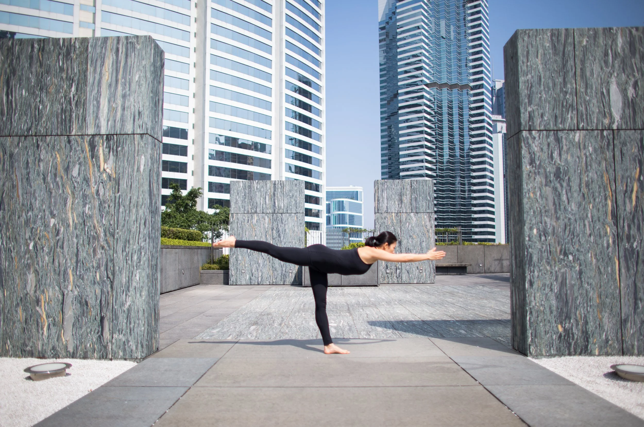 Woman practicing yoga in a warrior pose outdoors on a city rooftop with modern skyscrapers in the background.