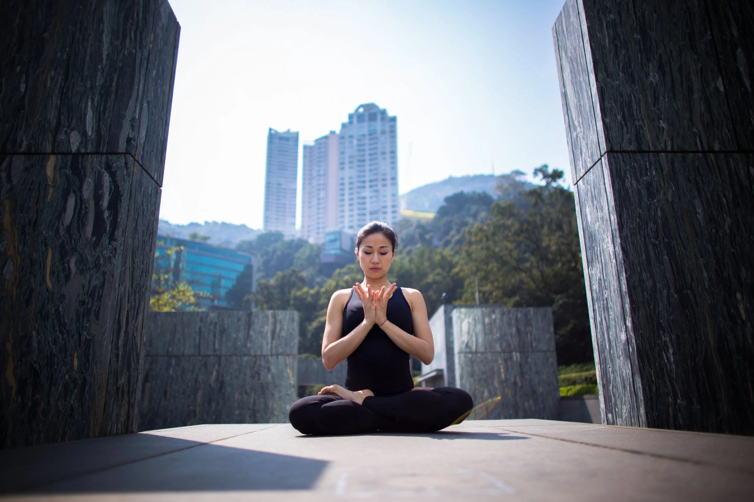 Woman practicing yoga outdoors on a platform with a cityscape and forested hills in the background.