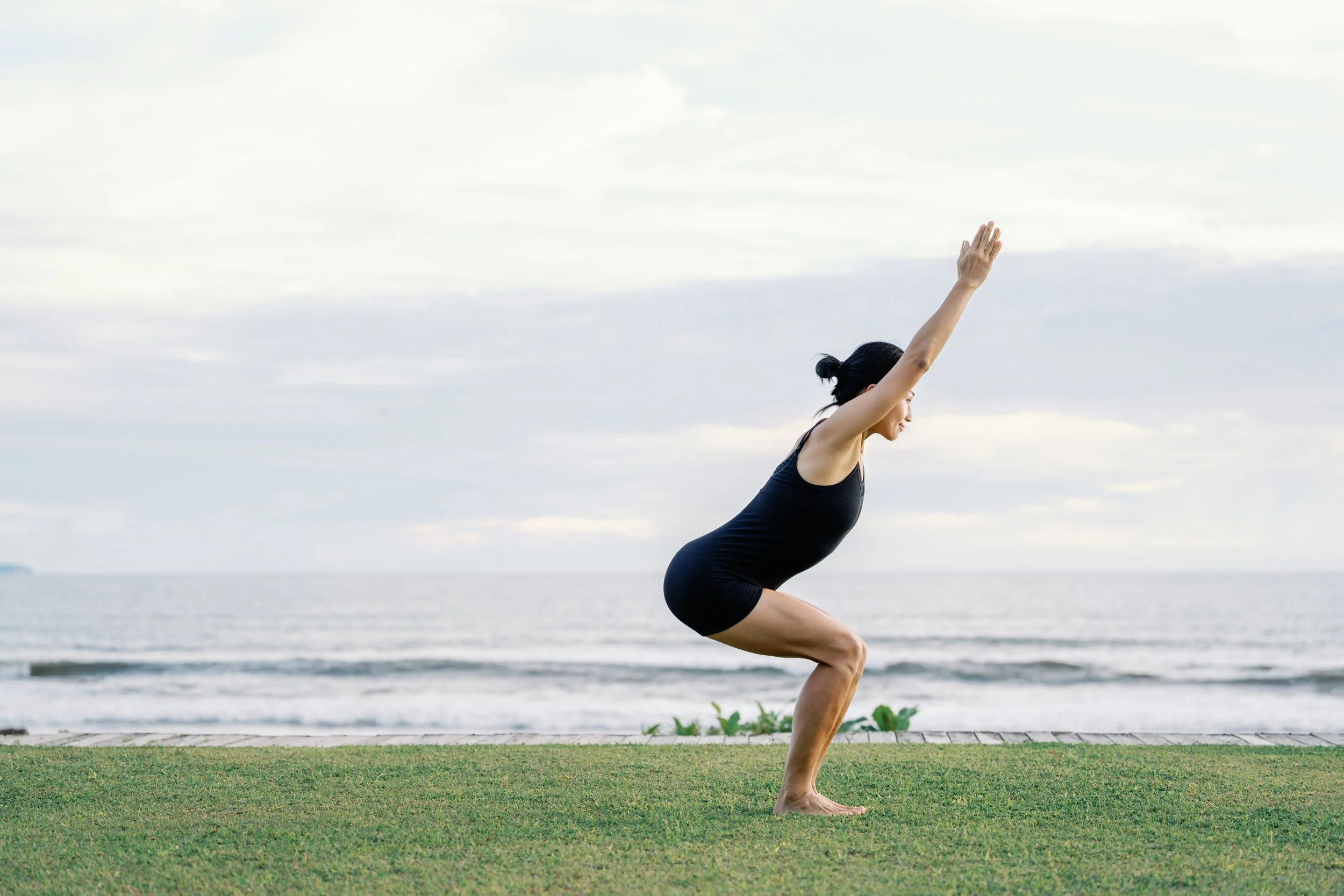 A woman doing yoga outdoors near a body of water during cloudy weather.