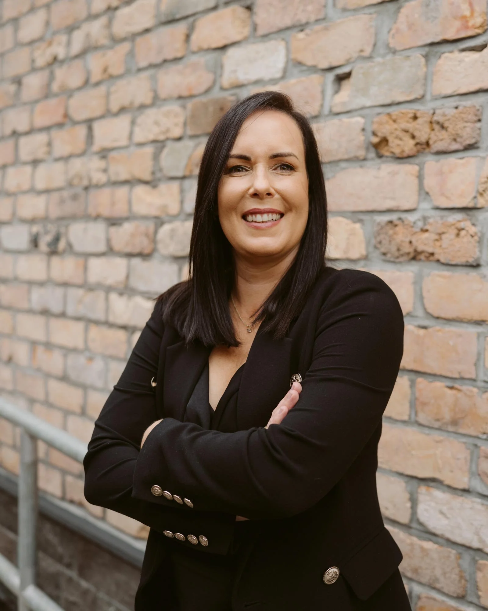 Claire McArthur standing with folded arms, in front of The Advisory office's brick wall