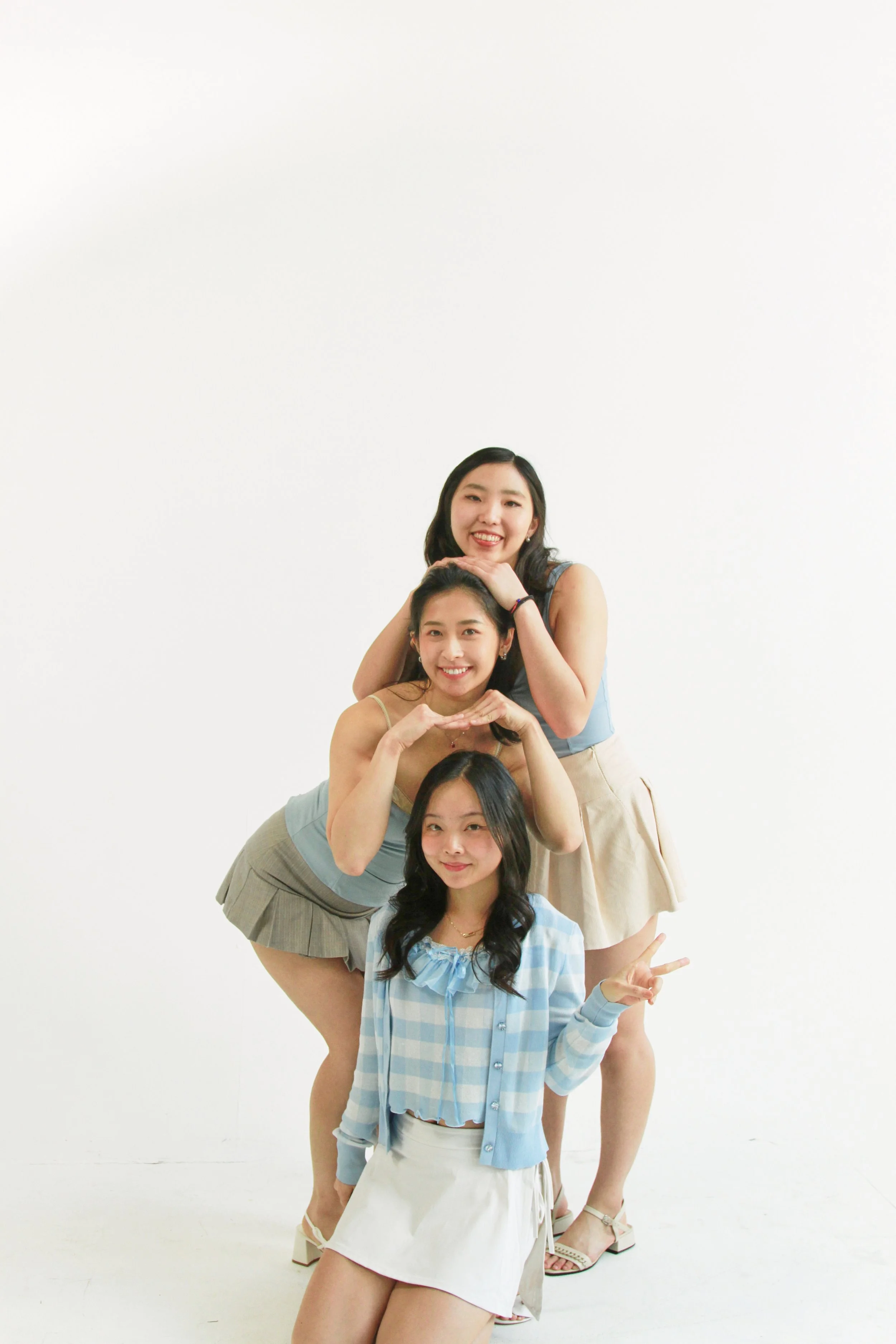 A group of five young women posing together in a playful, human pyramid formation against a plain white background. They are smiling and making fun gestures.