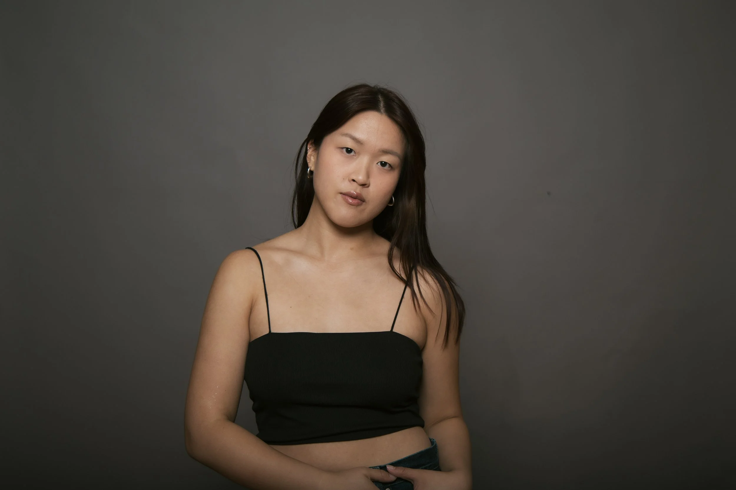 Young woman with dark hair in a black spaghetti strap top against a gray background.