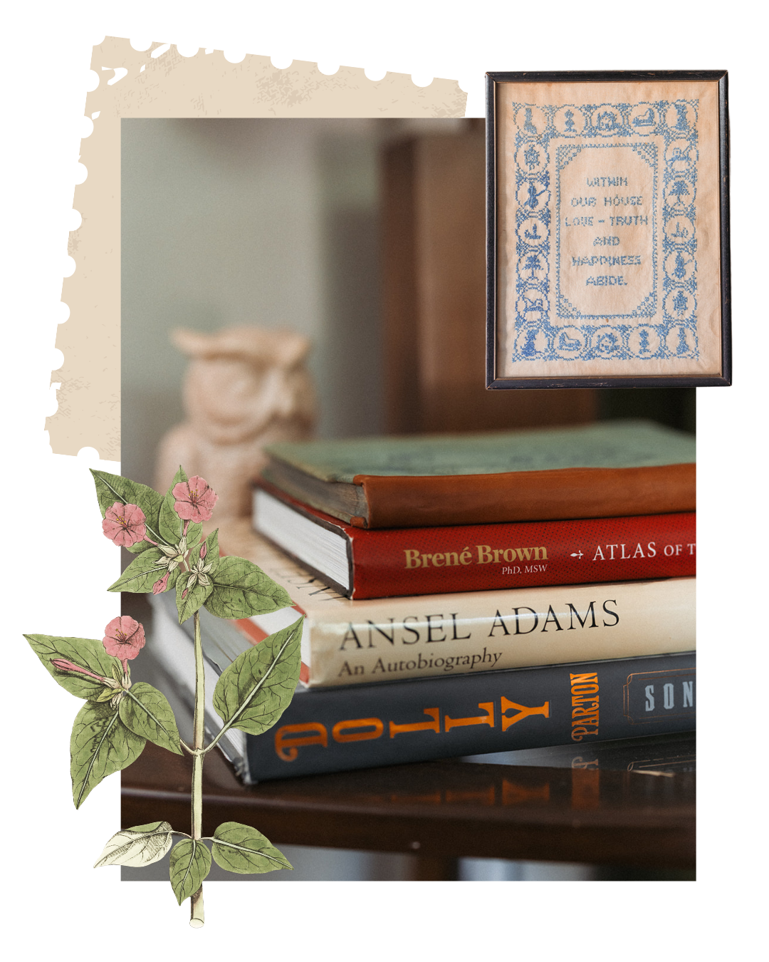 Stack of four books on a wooden surface with a framed embroidery hanging above. The books include 'Atlas of the Body' by Brené Brown, 'An Autobiography' by Ansel Adams, 'SON' by Peterson, and a book with a green cover. There is a plant with pink flowers and green leaves in the foreground. A blurred decorative object is in the background.