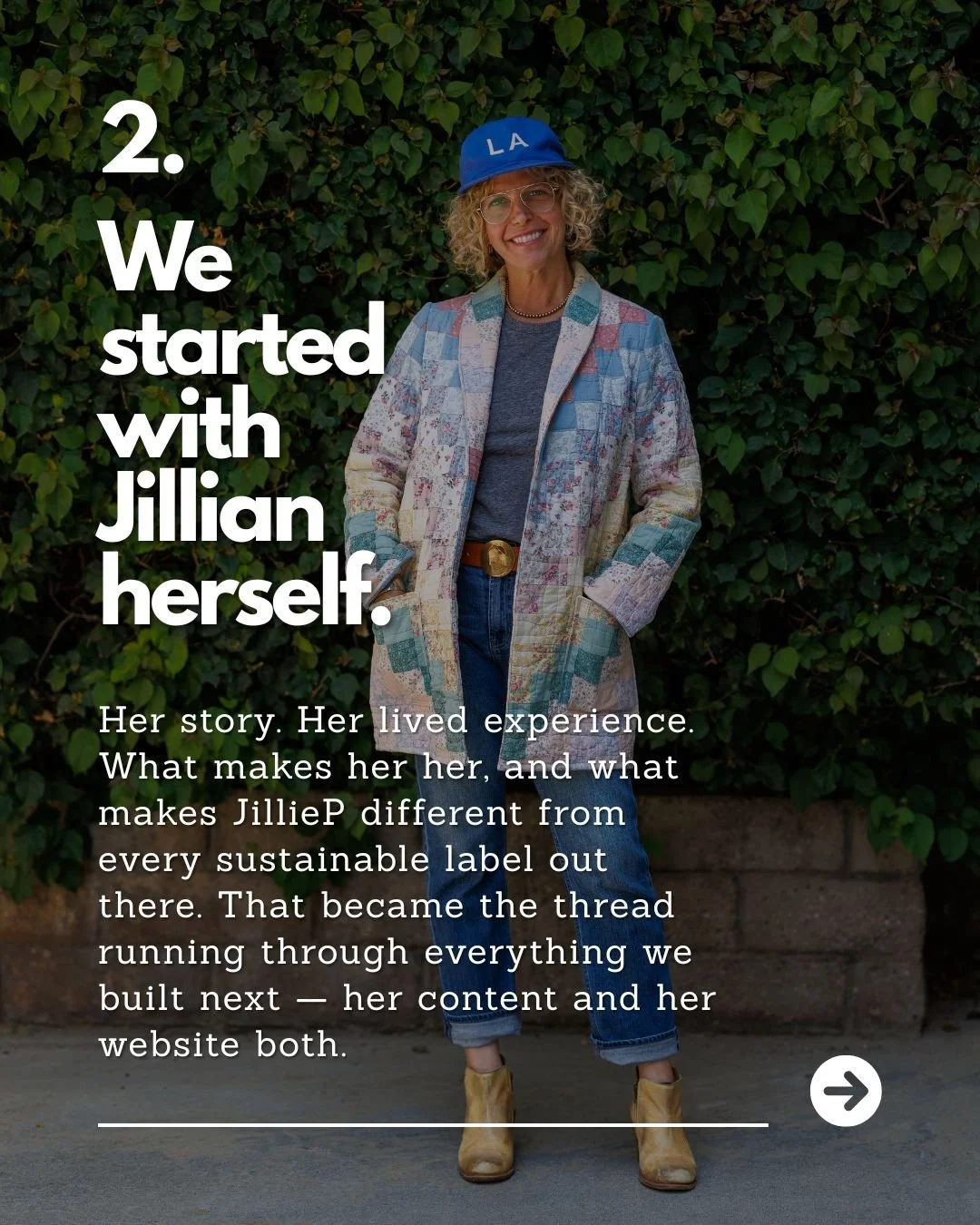 A woman with curly blonde hair, glasses, and a blue LA baseball cap, standing outdoors in front of lush green shrubbery. She is wearing a colorful patched blazer over a gray shirt, blue jeans, and tan ankle boots. She is smiling with her hands in her pockets.