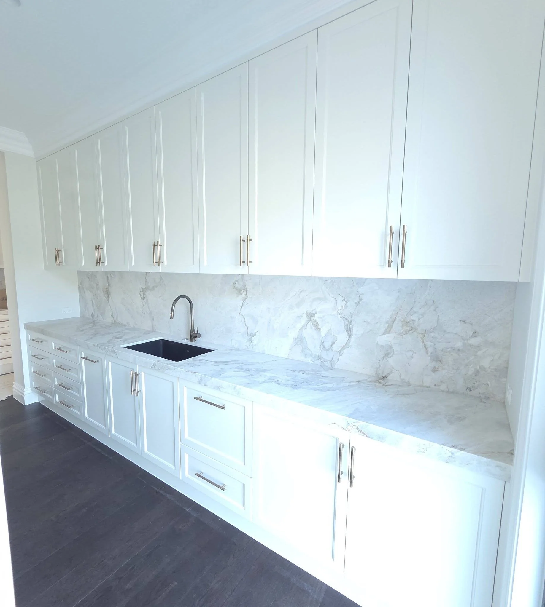 Modern kitchen with white cabinets and marble countertops, including a black sink and brass handles.