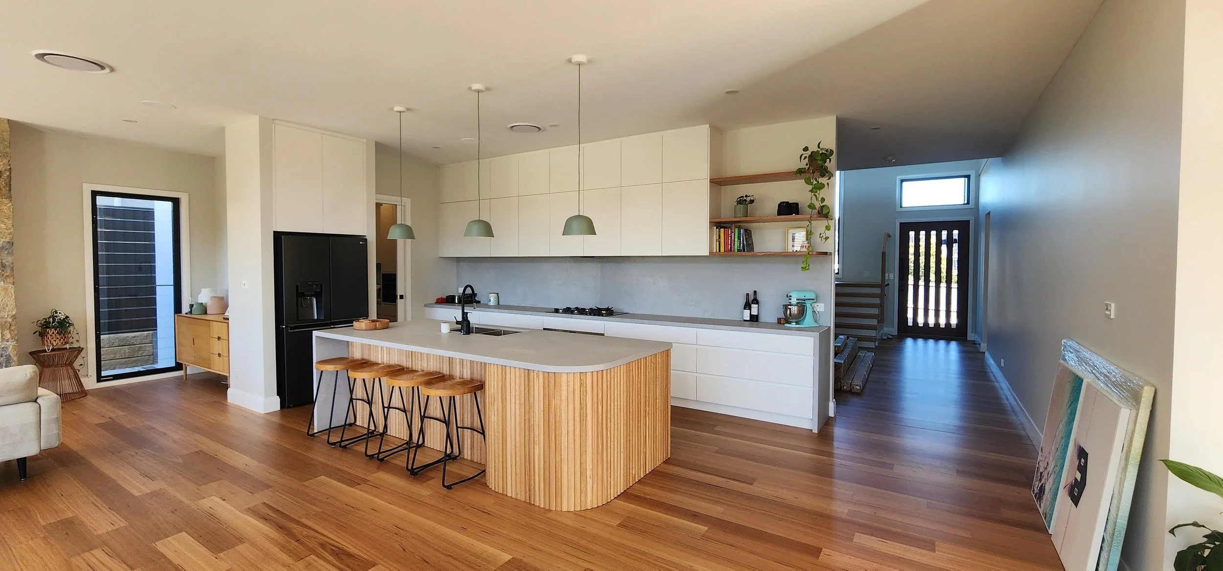 Open-concept kitchen with white cabinets, wooden island with seating, pendant lights, black refrigerator, and wooden flooring.
