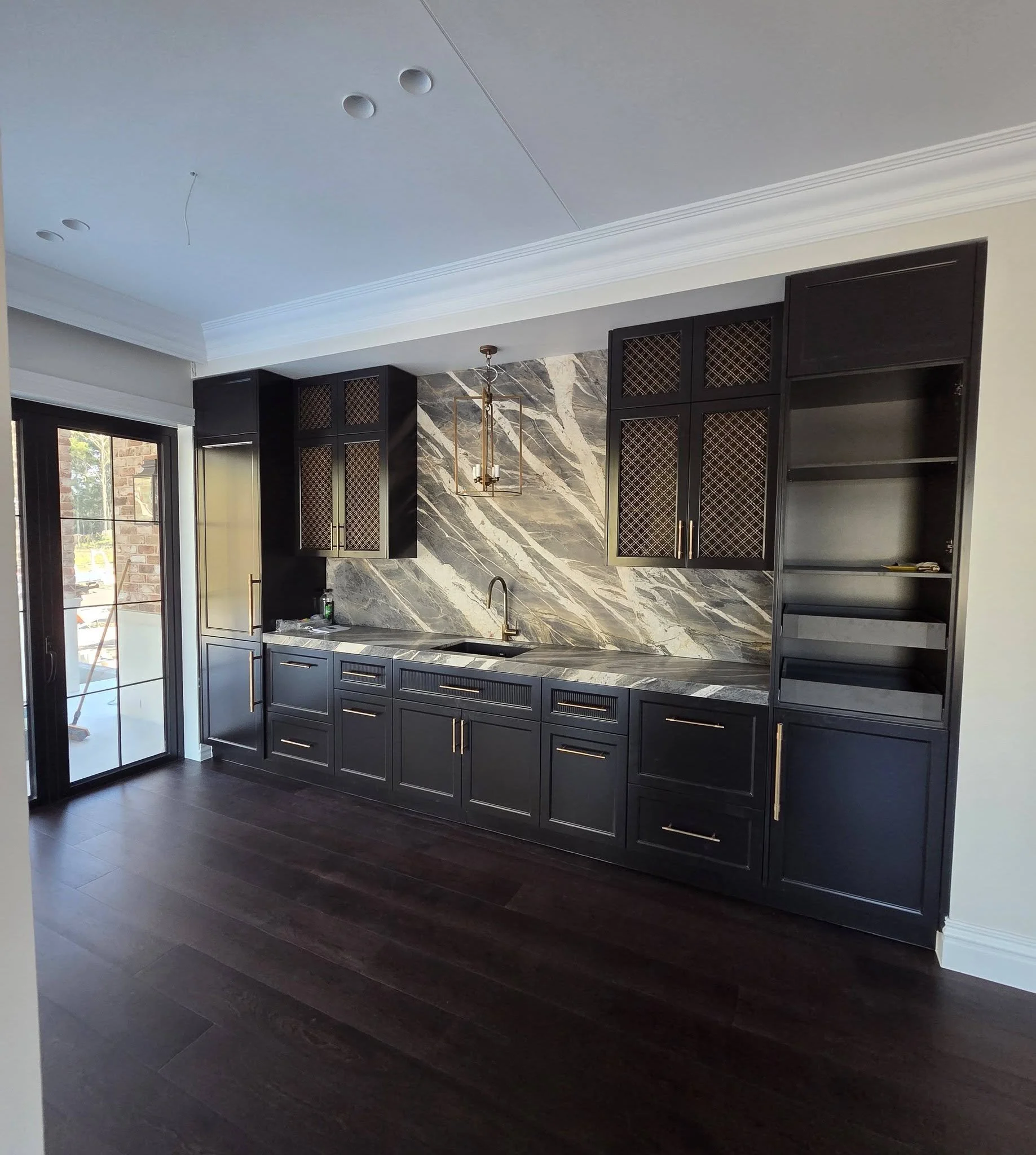 Modern kitchen with black cabinetry, marble backsplash, dark hardwood floors, and a sliding glass door.